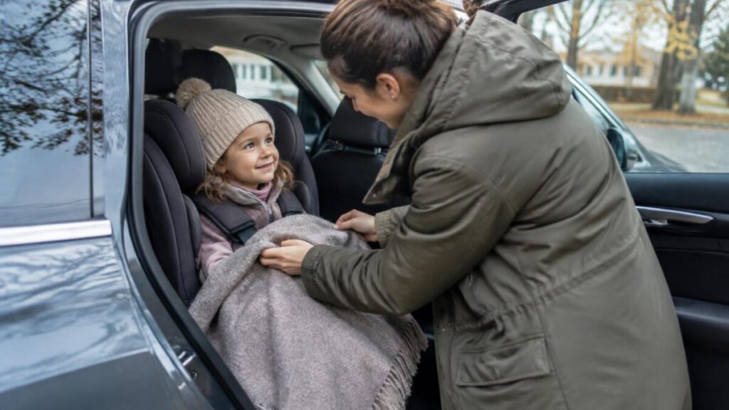 Rodič prikrýva dieťa pripútané v autosedačke dekou